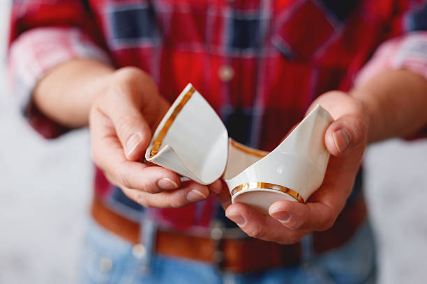 Man in plaid tartan shirt holds a broken white cup.