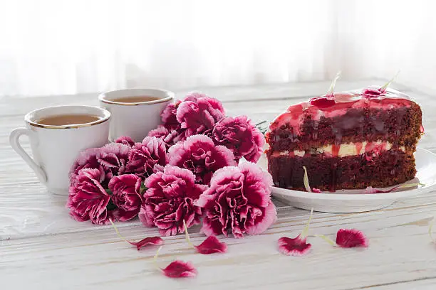 Red velvet cake, two cups of tea and pink carnations  on wooden table