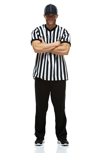 Full length profile shot of a football referee blowing a whistle and pointing with finger isolated on white background