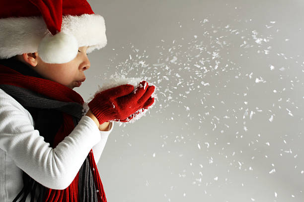 ragazzo in cappello di babbo natale fiocchi di neve soffiare - christmas child foto e immagini stock