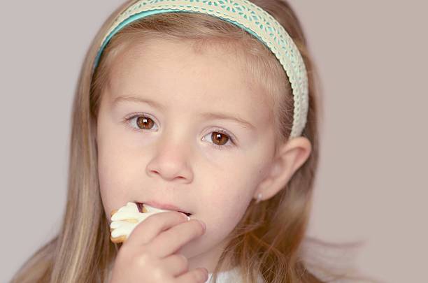 istock Cute girl eating cookie in form snowflake 525793319