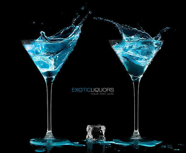 Two Cocktail Glasses with Blue Vodka. Style and Celebration Concept Ice cube between two cocktail glasses filled with blue alcoholic exotic liqueur splashing out, with copy space on black, concept of style and celebration. Template design with sample text ice cube photos stock pictures, royalty-free photos & images