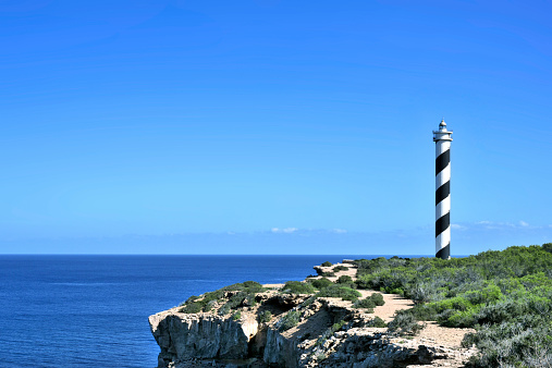 Lighthouse on a cliff. Rough coastline with blue sea and clear blue sky.