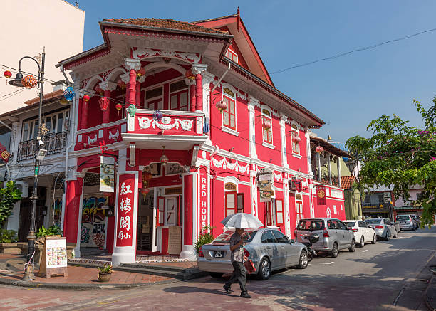 The Red House restaurant in Johor Bahru Johor Bahru, Malaysia - April 29, 2016: Corner house with a mixed colonial and Chinese style turned into a restaurant, the Red House. It is located in a calm street of Johor Bahru in Malaysia, with parked cars along the street. A man with an umbrella used as a parasol is walking by. The image was taken in the morning.  johor photos stock pictures, royalty-free photos & images