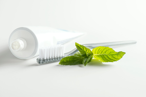 Toothpaste, brush and mint leaf on white background.