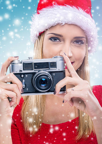 istock Beautiful woman with santa hat, holding the camera - snowfall 525829393