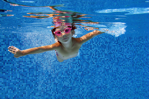 Happy child swims underwater in swimming pool. Kids sport