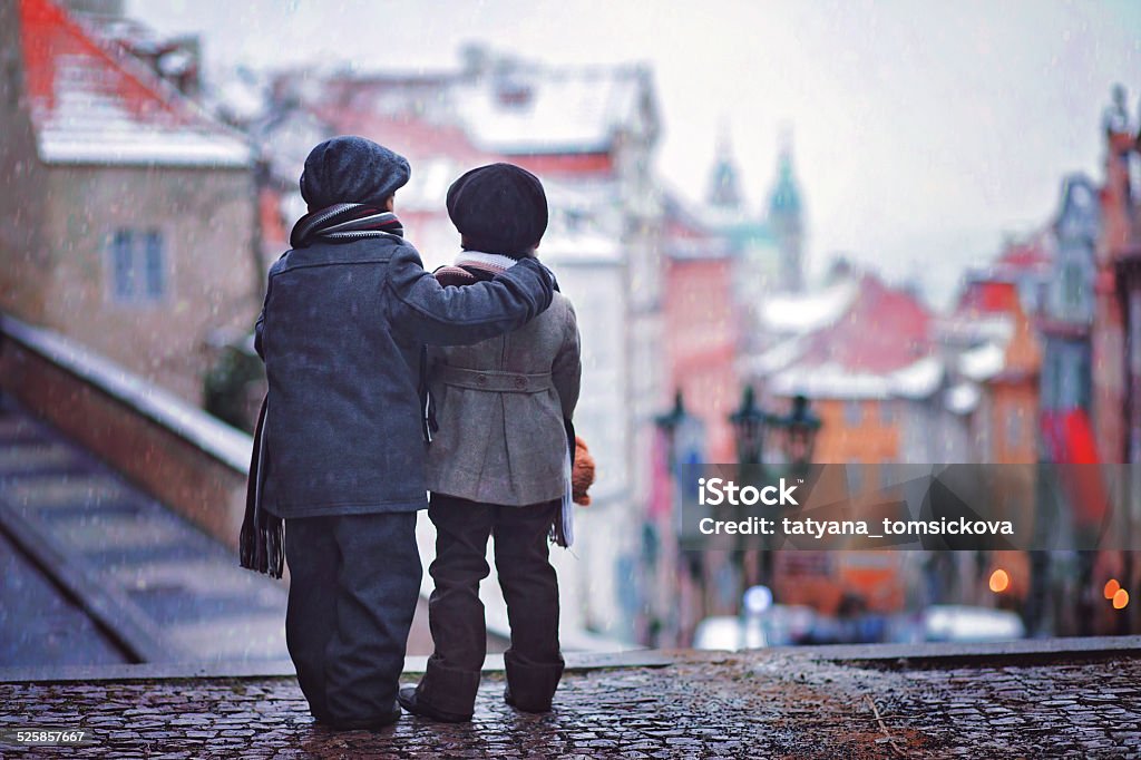 Two kids, standing on stairs, view of Prague behind them, Two kids, standing on a stairs, backwards, view of Prague in front of them, snowy evening Adventure Stock Photo