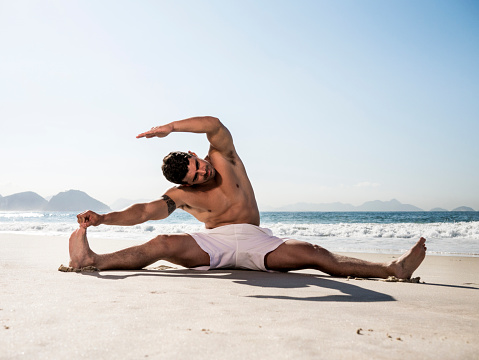 Hispanic man warming up on the beach before workout. Copy space.