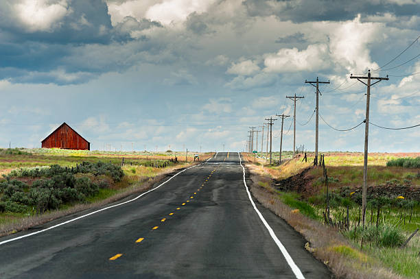 Red Barn and Road A lonesome highway in the Palouse area of eastern Washington State seems to lead to nowhere. A red barn can be seen in the distance. Power lines line the highway. east stock pictures, royalty-free photos & images