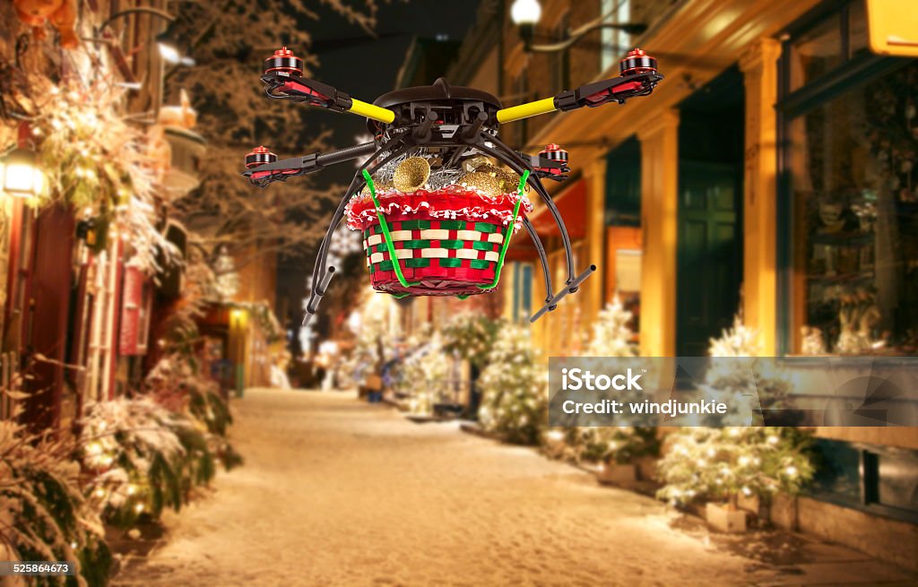 Aerial Christmas Delivery A flying quadrocopter delivering a basket of Christmas goodies above covered with snow beautifully decorated street Drone Stock Photo