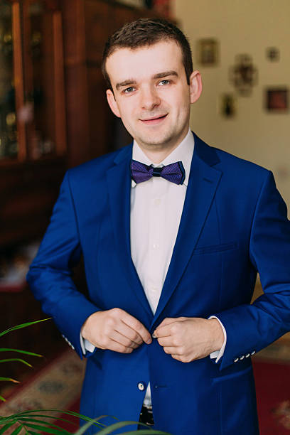 istock Adult solid man button his blue suit near window  looking 525878180