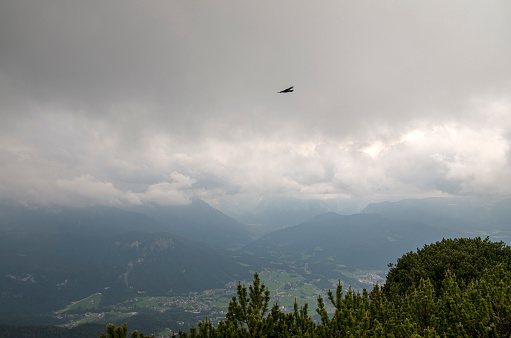 Eagle flying above cliff at the peak of a mountain with cloudy sky in the background.