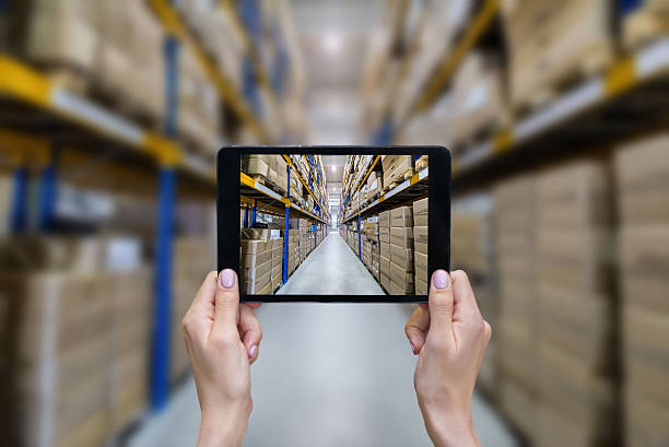 Ordering on-line from modern warehouse Horizontal color image of female hands holding a digital tablet in a corridor of futuristic distribution warehouse. Ordering online from a modern warehouse on a touchscreen tablet computer. Large distribution storage in background with racks full of packages, boxes, pallets, crates ready to be delivered. Logistics, freight, shipping, receiving. demanding photos stock pictures, royalty-free photos & images