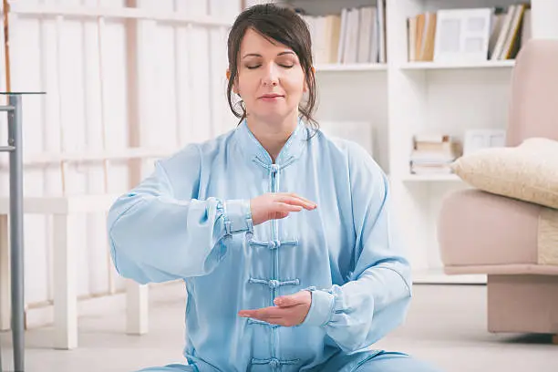 Beautiful woman doing qi gong tai chi exercise or reiki wearing professional, original Chinese clothes at home