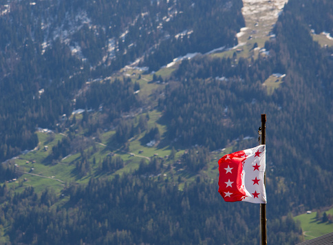 The red and white flag of Valais in Switzerland with a green valley in the background.