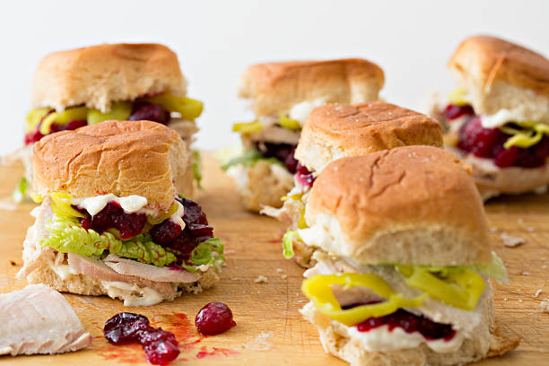 Mini Turkey Sandwiches A close up horizontal shot of several miniature turkey sandwiches made from sliced leftover thanksgiving turkey, cranberry sauce, mayonnaise, lettuce, deli sliced pepperoncinis and sweet Hawaiian honey wheat rolls. The white background provides some copy space on the top of the picture leftovers photos stock pictures, royalty-free photos & images