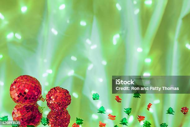 Red Christmas Ornaments And Confetti On Green Lit Background Stock Photo - Download Image Now