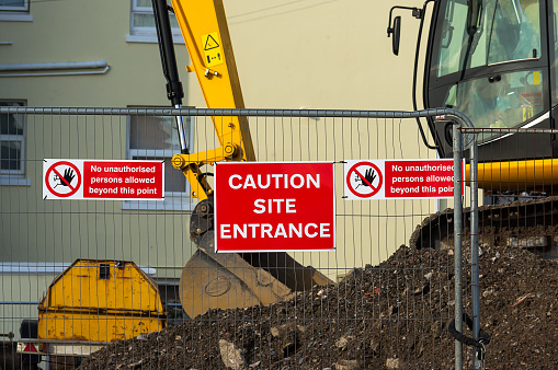 Caution sign at entrance to construction site.Red plaque hanging on the fence in the middle between the two arrays speaking about the ban on entry to the site.In the background you can see the construction site and construction machinery.