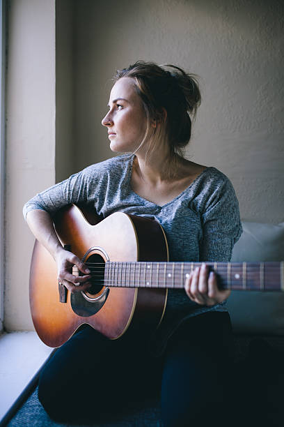 istock Girl sits by window playing guitar 525916341