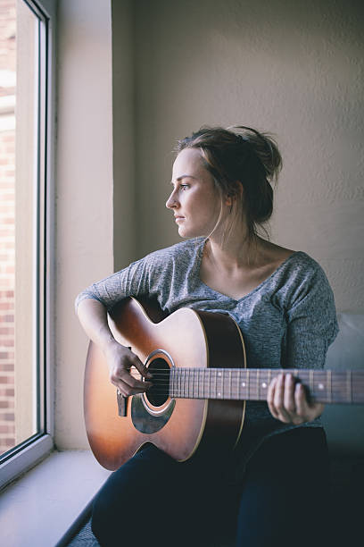 istock Girl sits by window and plays guitar 525916457