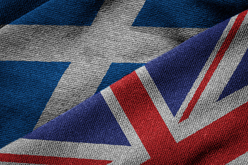 3D rendering of the flags of UK and Scotland on woven fabric texture. Concept of Scotland being part of the UK. Detailed textile pattern and grunge theme.