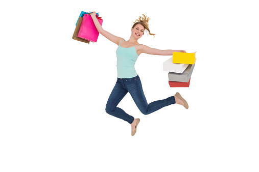 Excited blonde jumping while holding shopping bags on white background