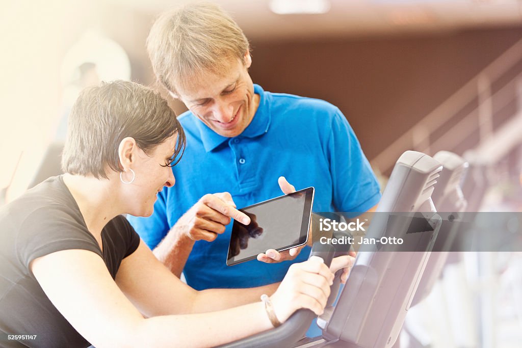 Trainer showing results of training on tablet PC to woman A fitness trainer, showing the results of the training to a woman on a tablet pc. She is listening concentrated. Both are smiling and having fun. Image taken with Canon EOS 1 Ds Mark II and EF 70-200mm USM L. 20-29 Years Stock Photo