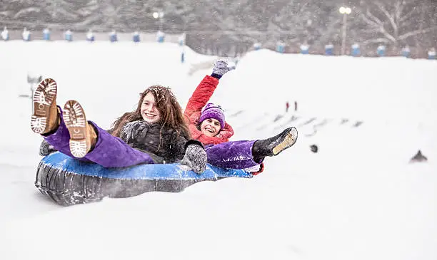 Two sisters, teenager girl and little girl, have fun with snowtubing at the winter resort 