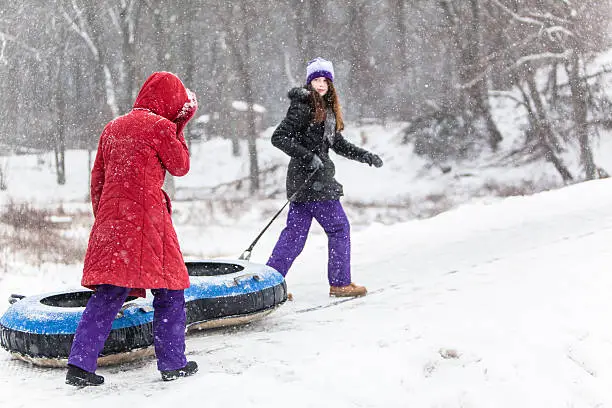 Two sisters have fun with snowtubing at the winter resort. They go to a hill top, oldest sister carry the tube. 