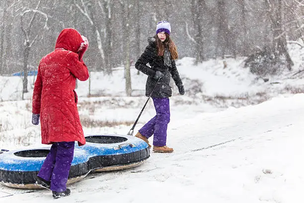 Two sisters have fun with snowtubing at the winter resort. They go to a hill top, oldest sister carry the tube. 