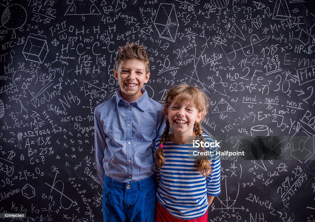 Happy boy and girl at school against big blackboard. Cute boy and girl at school in front of a big blackboard. Studio shot on black background. Back to School Stock Photo