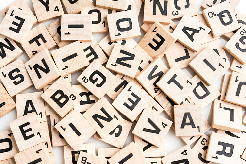 Miami, Florida,USA - April 10, 2014: Scrabble game piece letter tiles scattered in random order from above on white background. Scrabble is a crossword strategy game distributed by Hasbro.