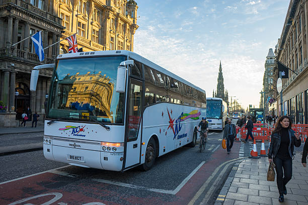 Edinburgh, Scotland - April 20, 2016: Princes Street, Edinburgh.  Coach driving down Princes street, another coach is behind.  People are just in shot walking down the street, including a cylist.  Scott Monument also is in shot.