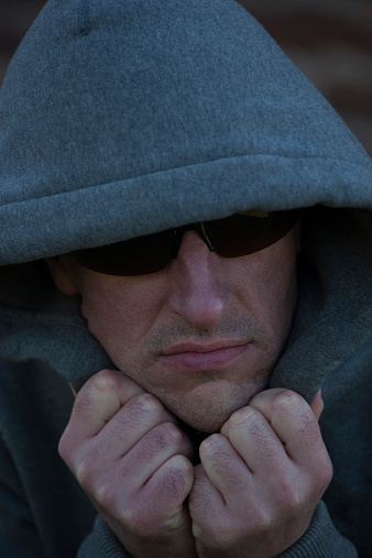 Man wearing hoodie and sunglasses with villainous appearance