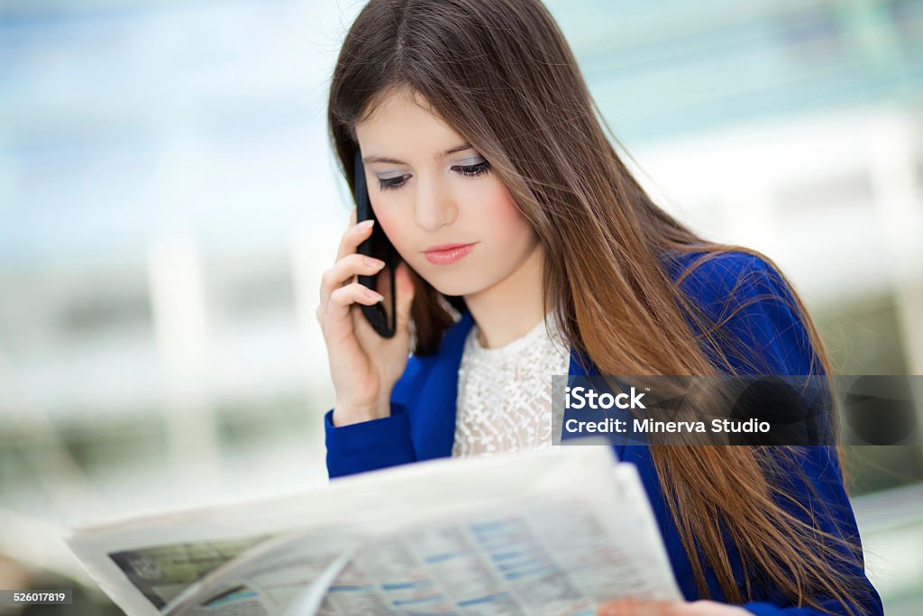 Smiling businesswoman talking on the phone Businesswoman talking on the phone and reading newspaper 20-29 Years Stock Photo