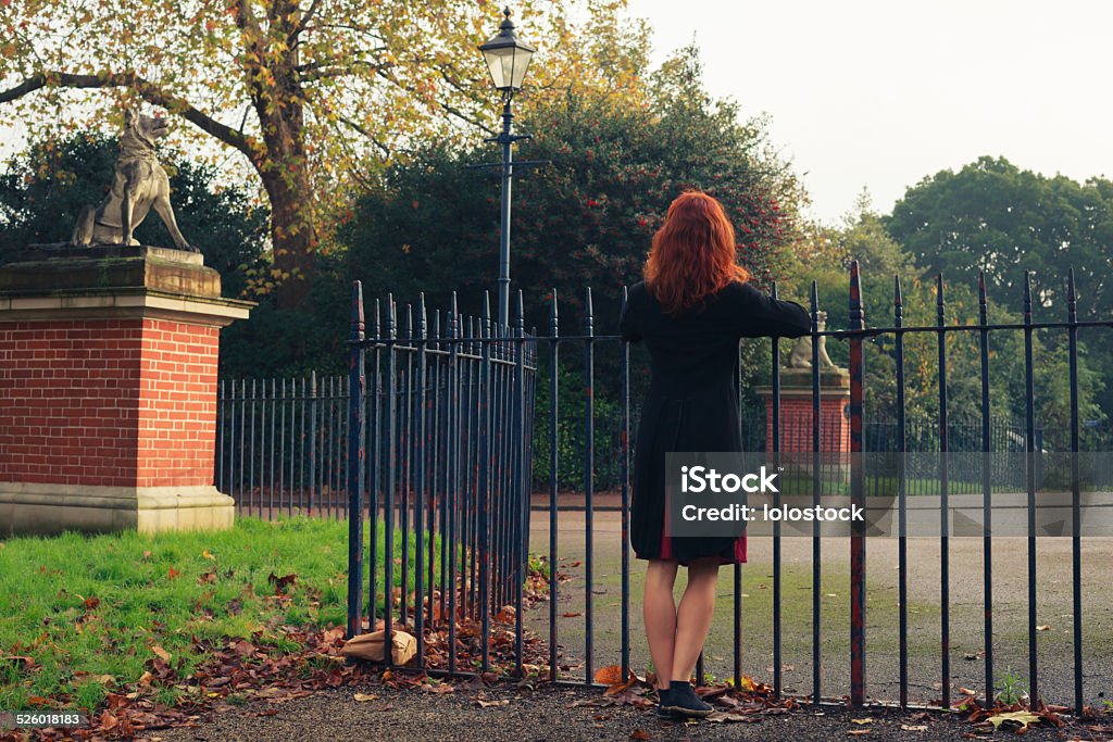 Woman leaning on gate in park A young woman is leaning on a gate in a park in the autumn Adult Stock Photo