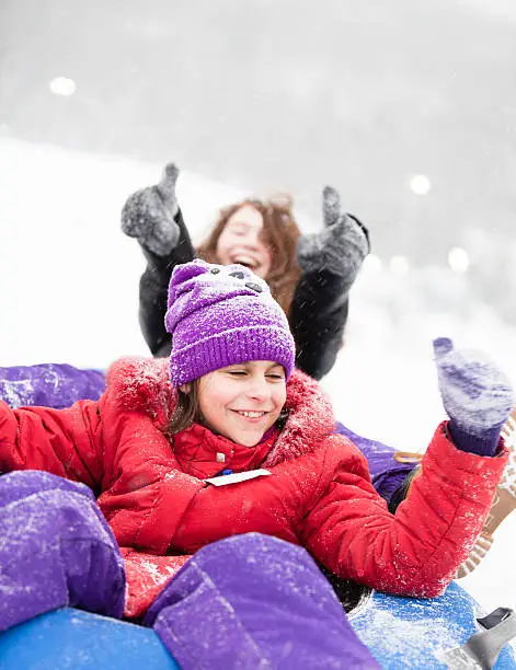 Two sisters, teenager girl and little girl, sliding at the slope and have fun with snowtubing at the winter resort 