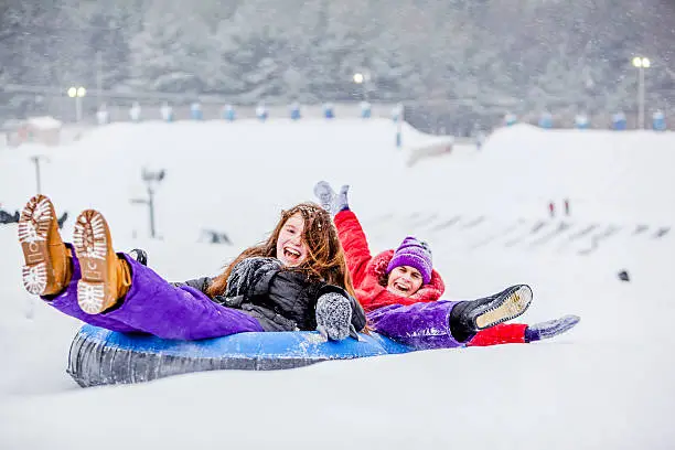 Two sisters, teenager girl and little girl, have fun with snowtubing at the winter resort 