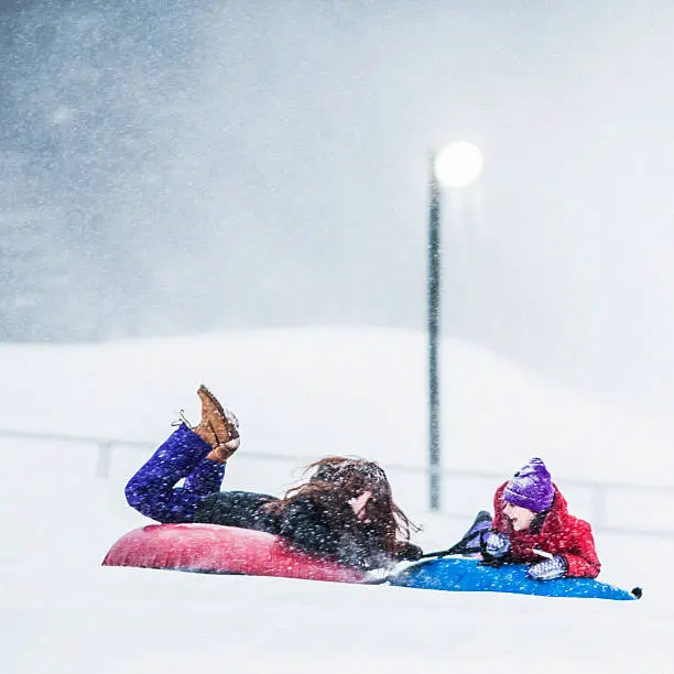 Two sisters, teenager girl and little girl, sliding at the slope and have fun with snowtubing at the winter resort 