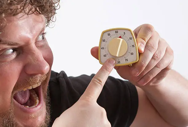 A man hold a eggtimer in his hands. Man in the background is unsharp. His eyes are big.