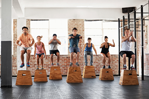 Shot of a group of people jumping onto boxes in a gym class