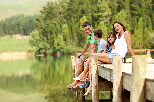 Shot of a family sitting on a pier by the lake