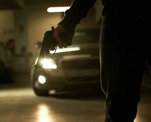 A criminal holding a revolver about to hijack someone in an underground parking lot