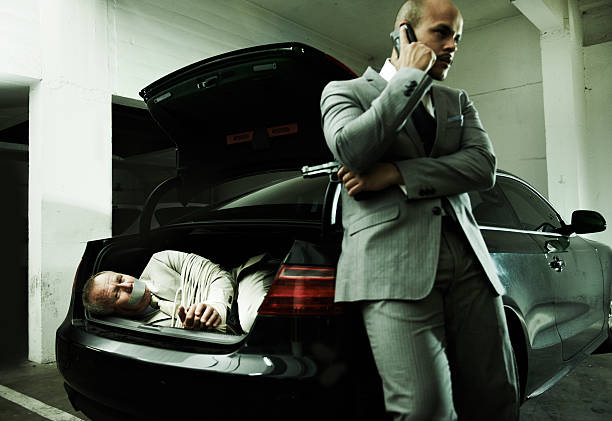 We got the big one, boss A frightened businessman lying in the trunk of a car while his captor talks on a cellphone trapped fear people business stock pictures, royalty-free photos & images