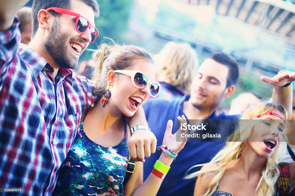 People enjoying concert party. Group of people enjoying a concert,closeup.There's mid 20's couple in focus with his arm raised and wearing sungless.Having big smiles on their faces. Blurry people in background. 20-29 Years Stock Photo