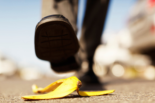 An unidentified  male walker's foot in a formal shoe is about to step on a dropped banana peel - a painful accident waiting to happen! Focus on the banana skin.