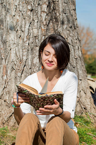 istock Beautiful young woman reading a book on tree background 526070955