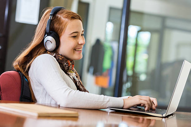 istock Preteen girl doing homework on laptop while using headphones 526086865