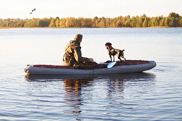 Photo of The hunter with a dog in the boat in the middle of the lake